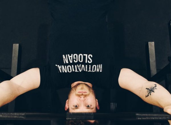 Bearded sportsman in t shirt with inscription exercising with weight while looking at camera